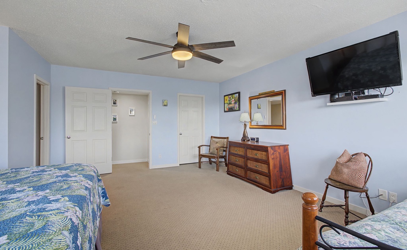 Your spacious bedroom features comfortable beds, warm blue walls, a ceiling fan, flat-screen TV, and classic wooden furnishings for a peaceful stay.