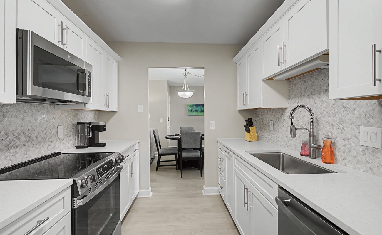 Your sleek galley kitchen features pristine white cabinets, marble backsplash, and stainless steel appliances—perfect for preparing memorable meals during your stay.