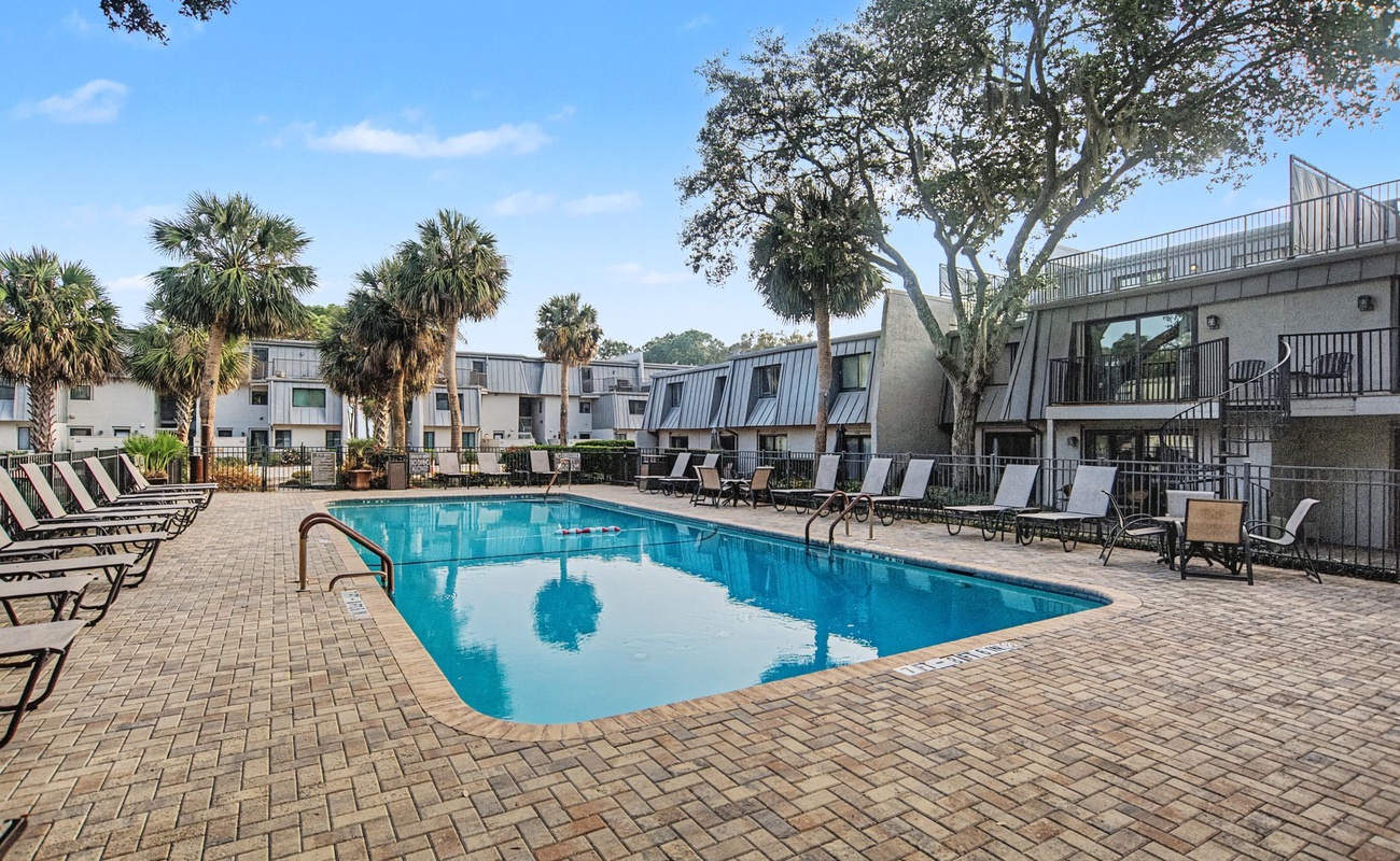 The property features a sparkling outdoor pool surrounded by comfortable loungers beneath swaying palm trees.