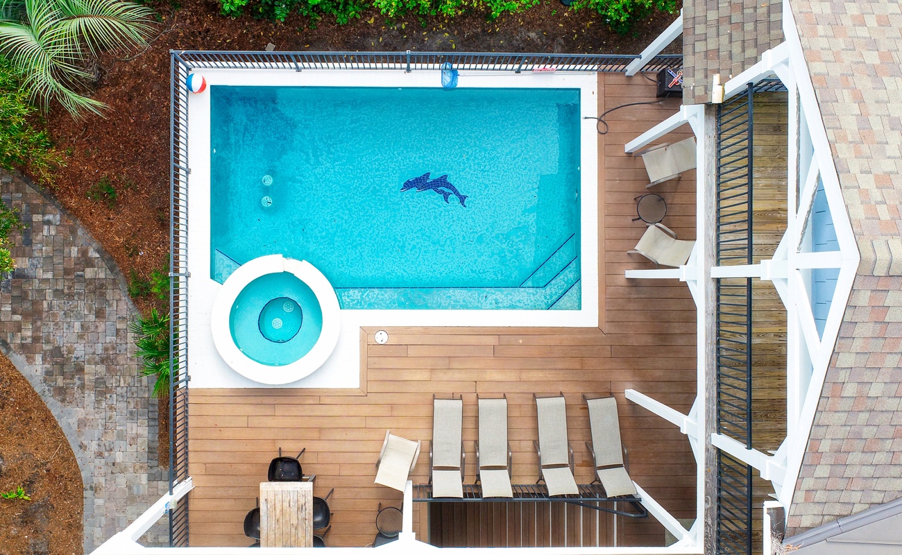 Your private pool awaits with crystal-clear water and a separate hot tub, surrounded by comfortable lounge chairs on warm wooden decking.