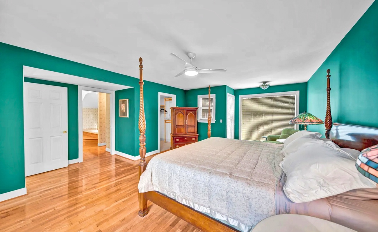 Wake up refreshed in your vibrant bedroom featuring gleaming hardwood floors, elegant four-poster bed, and calming turquoise walls that create a truly unique retreat.