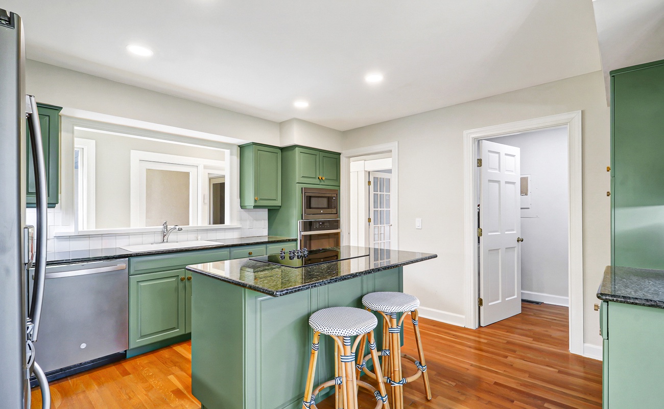 The fully-equipped kitchen features sage green cabinets, granite countertops, and a breakfast bar perfect for morning coffee or casual meals.