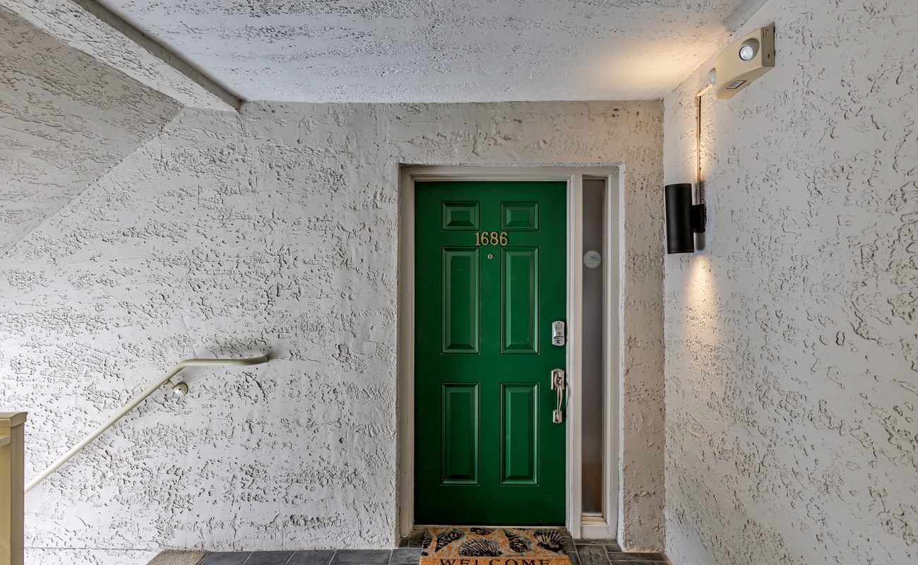 A welcoming green door marked 1686 greets you at this charming entrance, complete with warm lighting and a friendly welcome mat.