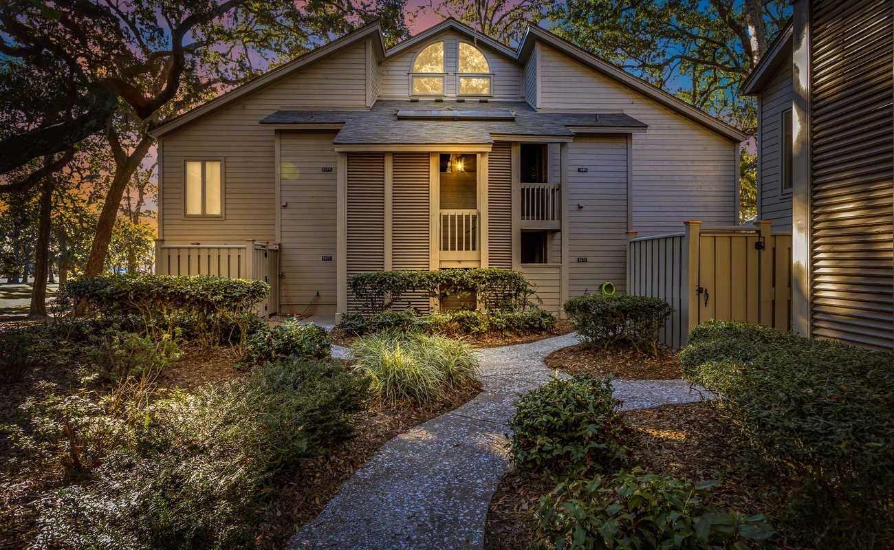 Charming property exterior featuring warm lighting and landscaped grounds at dusk.