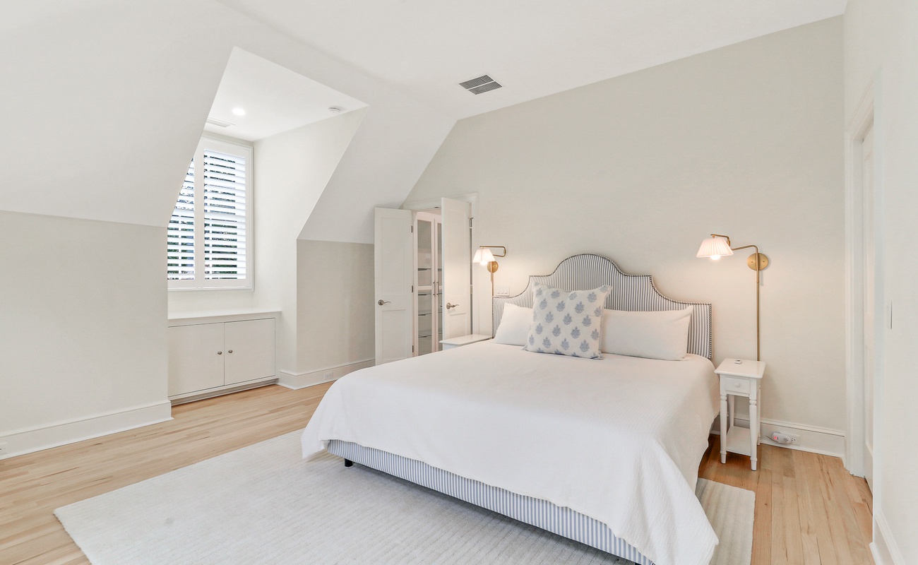 Relax in your bright attic bedroom with cozy lighting, elegant furnishings, and peaceful white linens for restful nights.