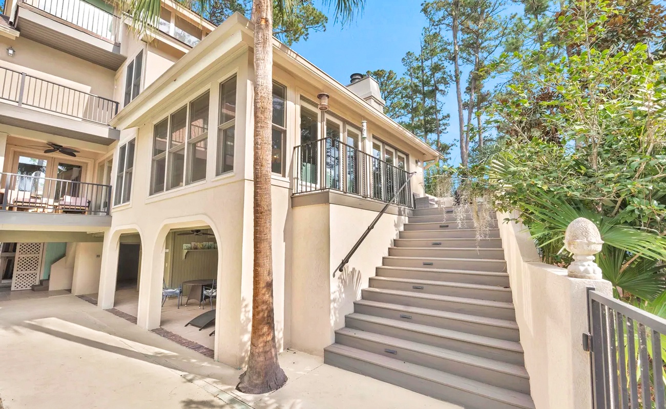 Elegant coastal architecture nestled among towering pines and palms, featuring expansive terraces and tropical surroundings.