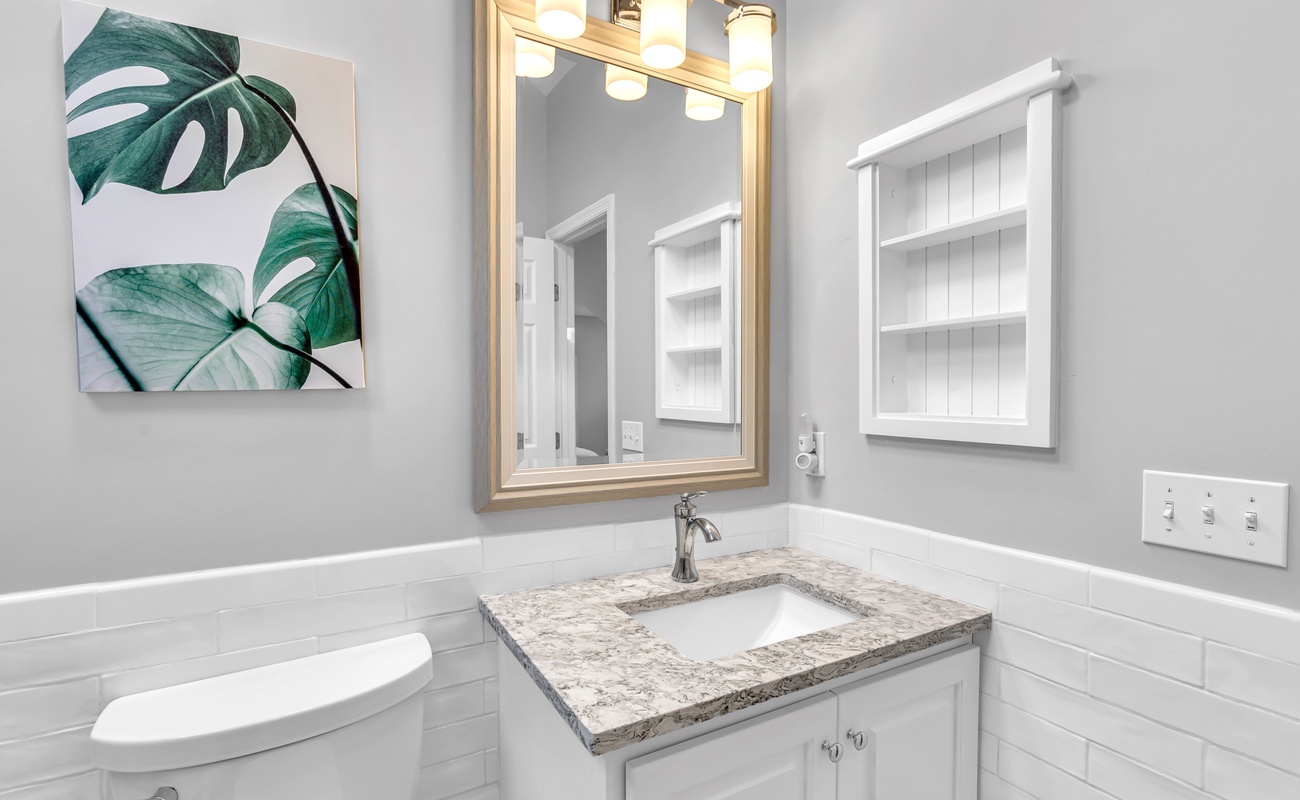 Refresh in your beautifully appointed bathroom featuring elegant marble countertops, bright vanity lighting, and tropical artwork that creates a serene spa-like atmosphere.