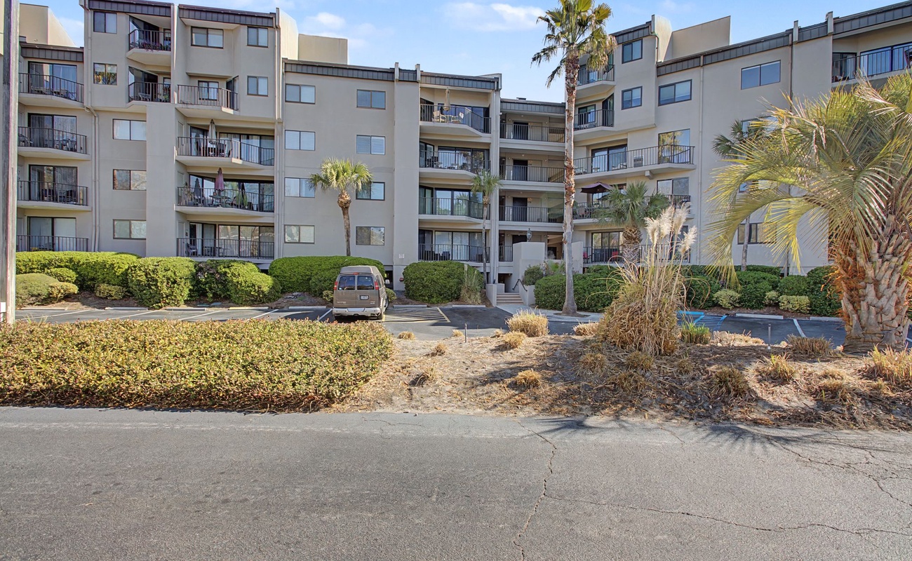 Modern apartment complex featuring multiple levels with private balconies, surrounded by tropical palm trees and landscaped grounds with convenient parking access.