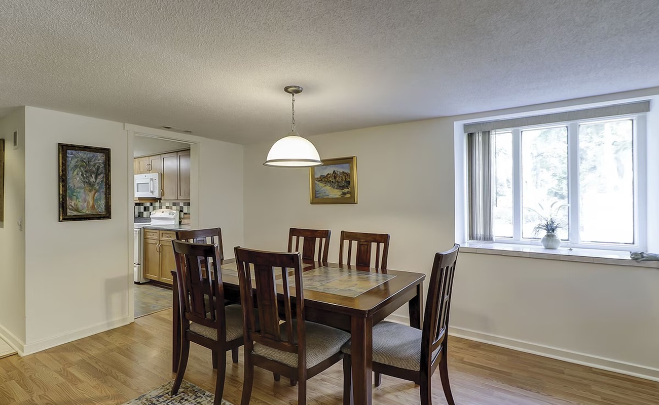 Your spacious dining area features a beautiful wooden table where you'll share memorable meals together, with natural light streaming through large windows.