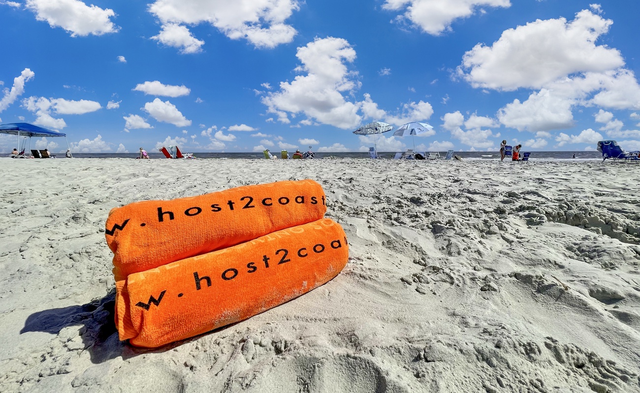 Sandy beach with colorful umbrellas and beachgoers enjoying a perfect day under brilliant blue skies and fluffy white clouds.