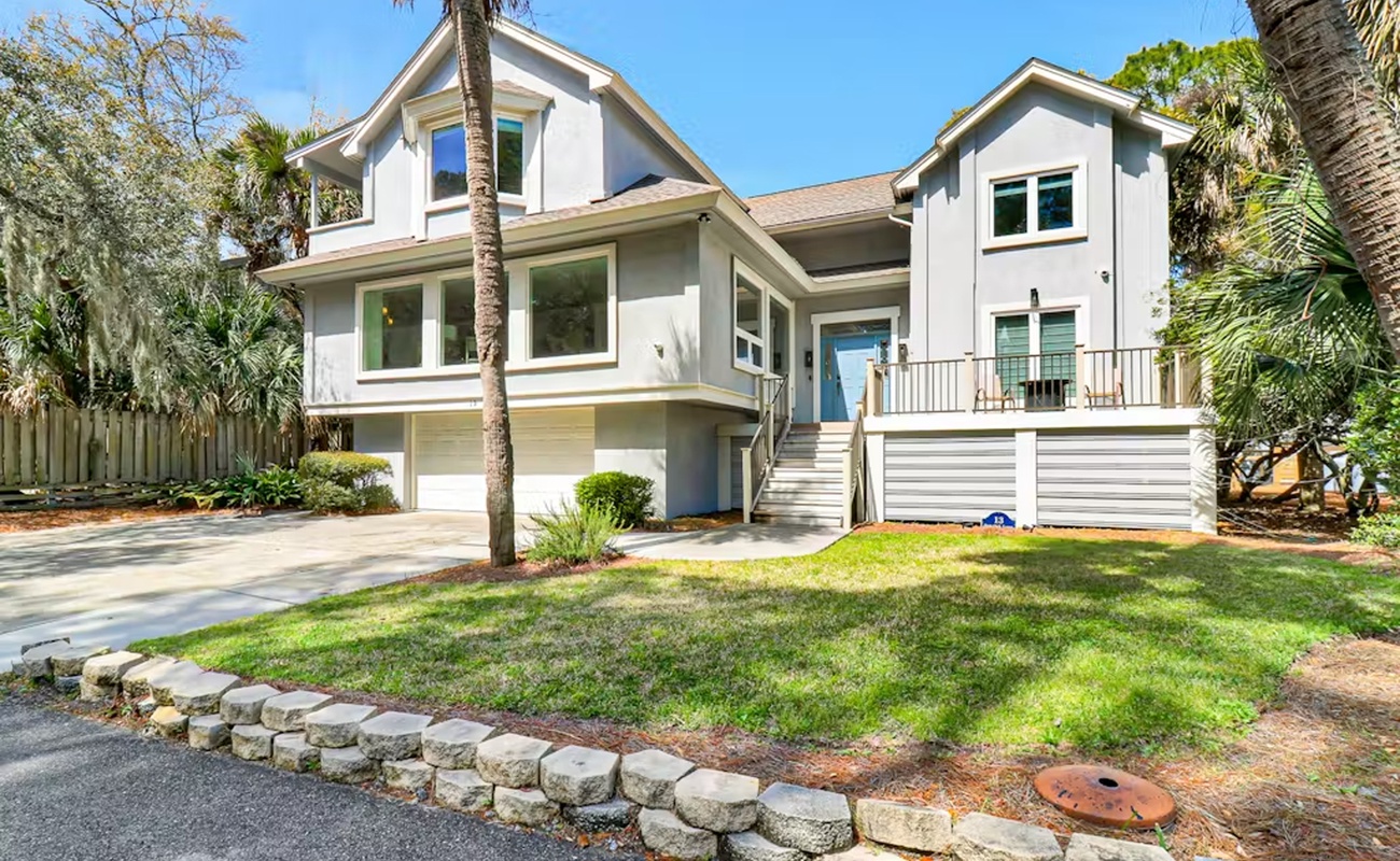 Modern two-story coastal home surrounded by lush palm trees and tropical landscaping.