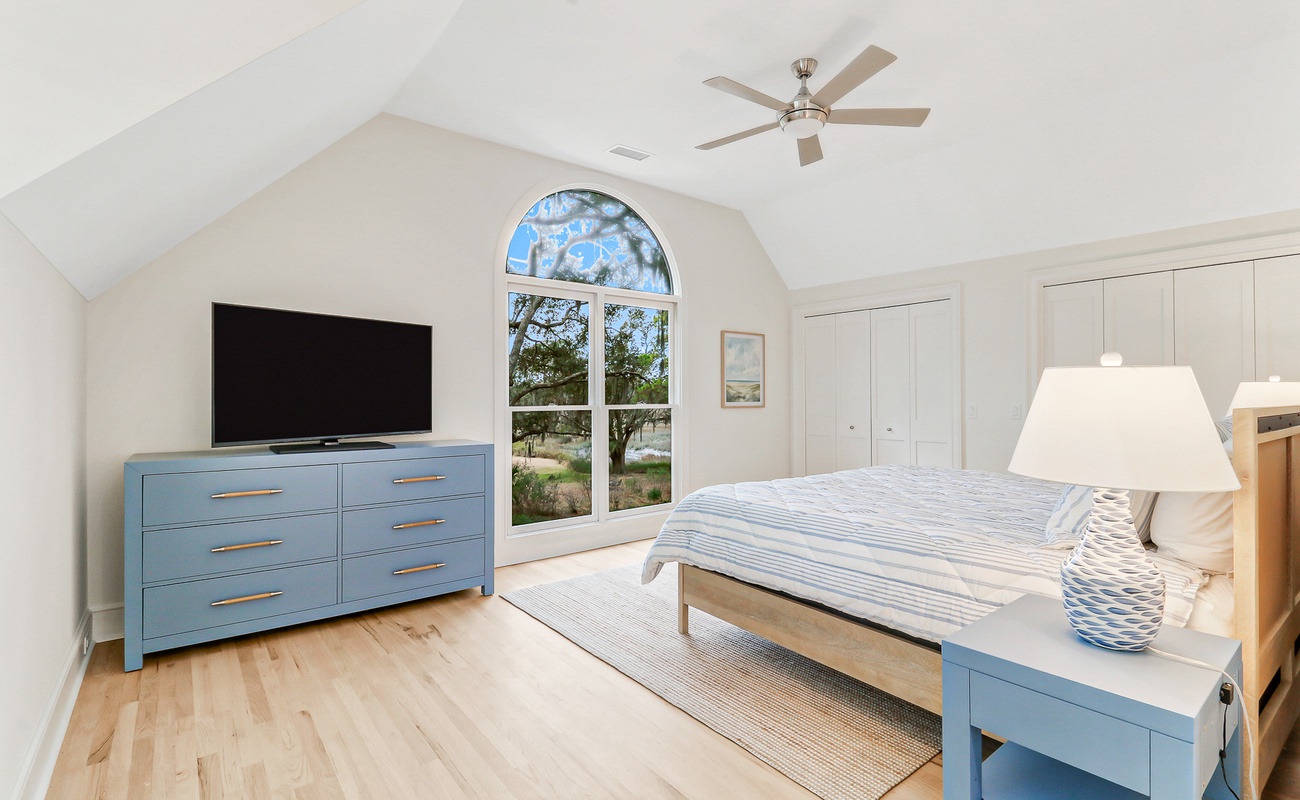 Unwind in this serene bedroom featuring soothing blue accents, vaulted ceilings, and peaceful garden views through arched windows.