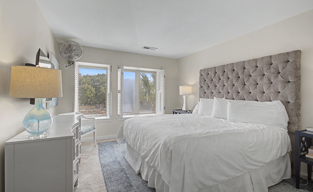 Sink into crisp white linens beneath this stunning tufted headboard, while natural light streams through your windows overlooking lush greenery.
