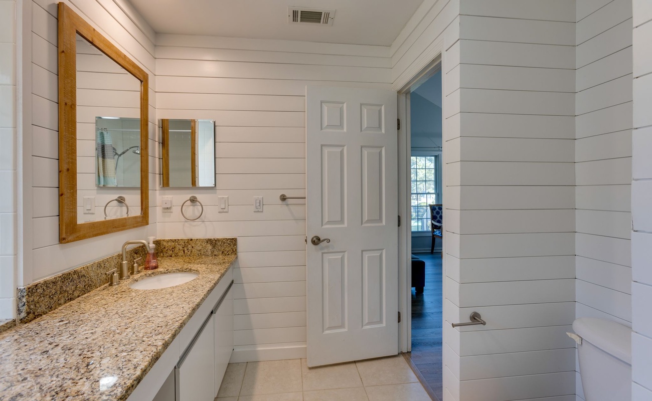 Step into your stylish bathroom featuring shiplap walls, granite countertops, and warm wood-framed mirrors that create a perfect coastal-modern retreat.