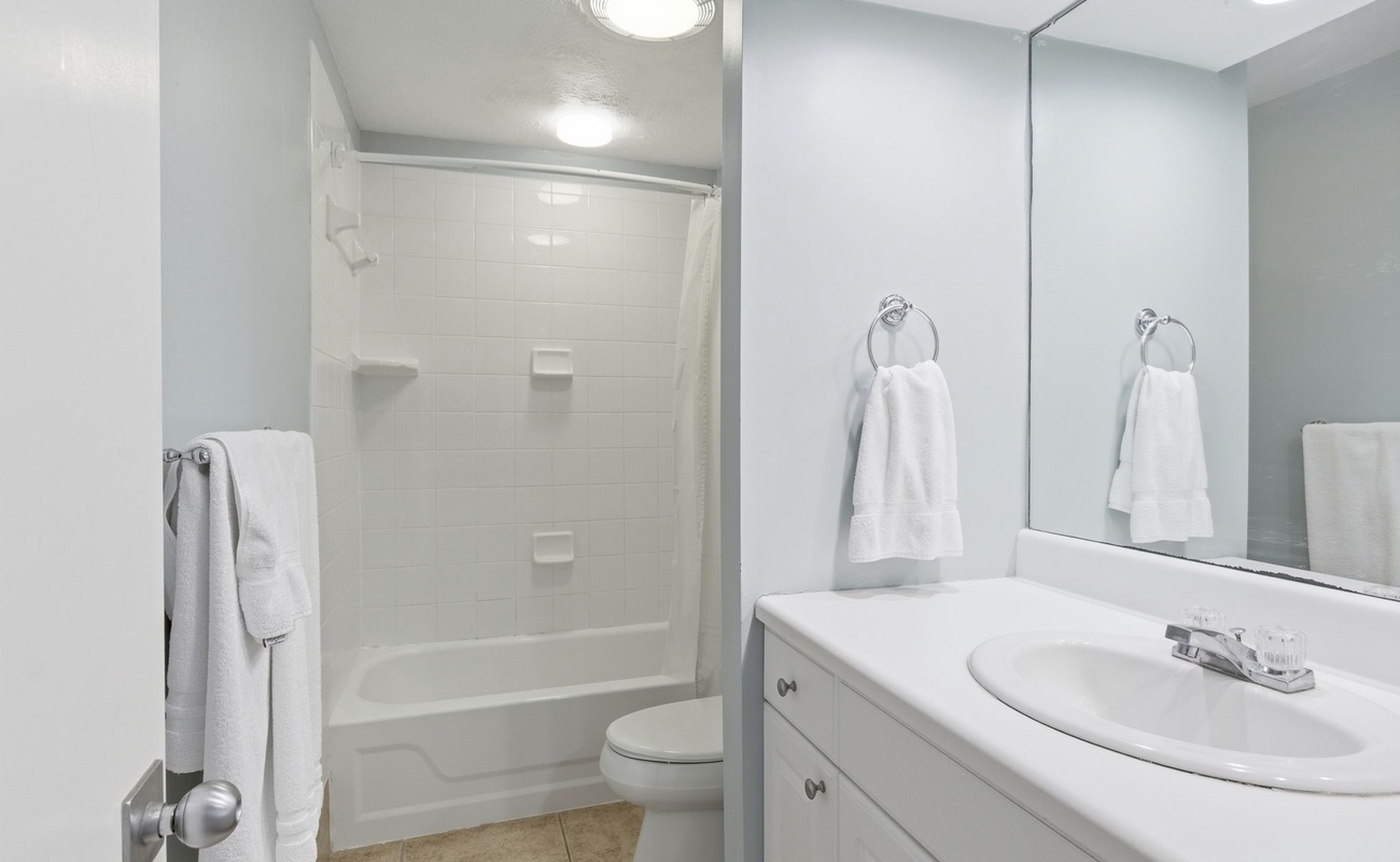 Fresh white bathroom with tub-shower combo and plush towels waiting for your relaxing soak.
