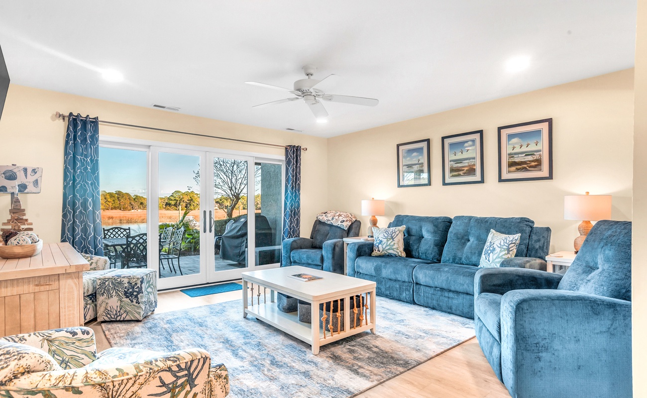 Relax in your spacious living room with plush blue seating, coastal decor, and serene views through sliding doors to your private outdoor space.