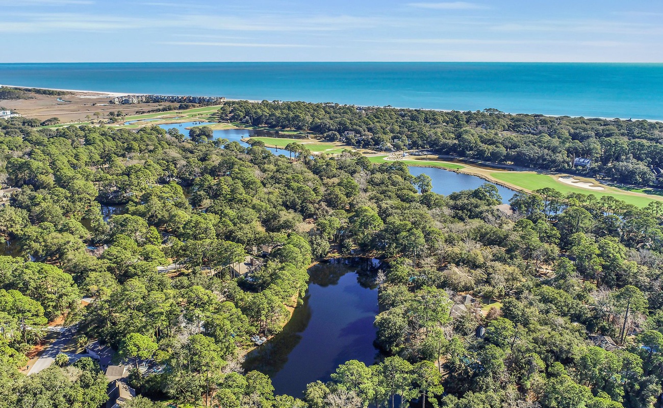Stunning aerial view showcases the coastal property's prime location, nestled between pristine beaches and championship golf course fairways with scenic water features.