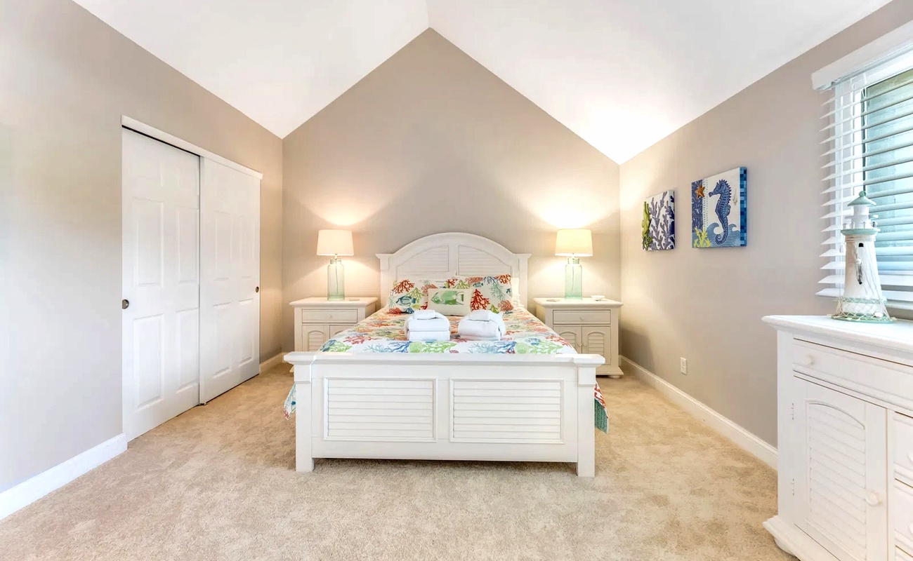 Drift off in this peaceful bedroom with soft carpeting, charming coastal decor, and warm bedside lighting creating your perfect retreat.