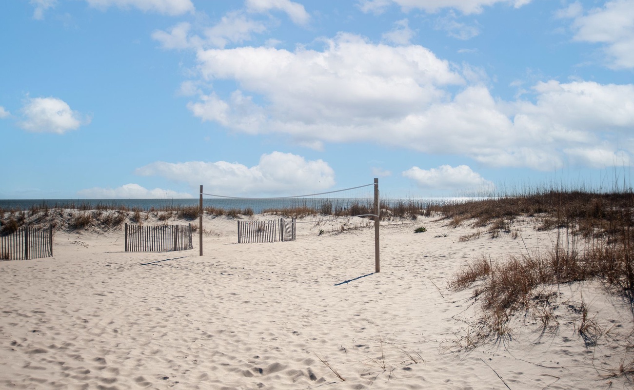 Protected sandy beach area with dune fencing and natural vegetation under partly cloudy skies.