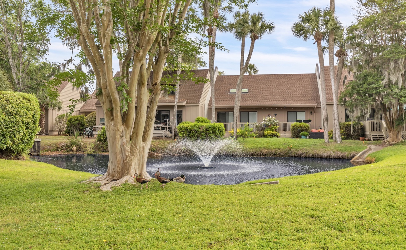 Peaceful waterfront property surrounded by lush landscaping and mature palm trees with fountain water feature.