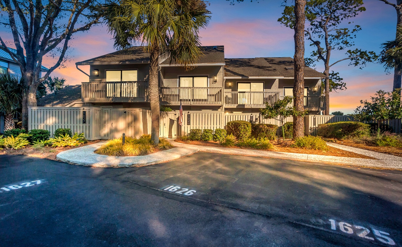 A beautifully landscaped property entrance with tropical palms and warm lighting welcomes guests as twilight paints the sky in stunning hues.