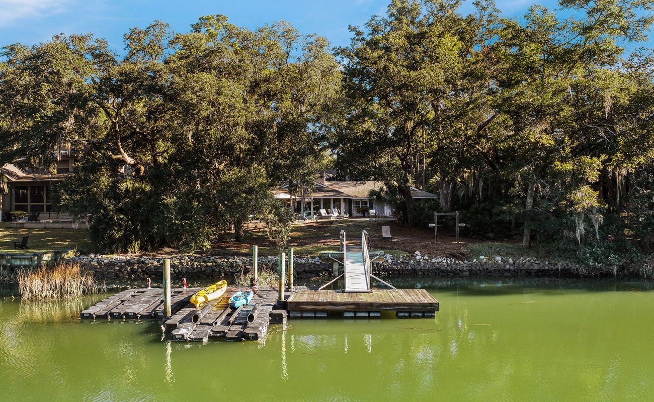 Waterfront property with private dock and kayaks on serene lake surrounded by mature trees.