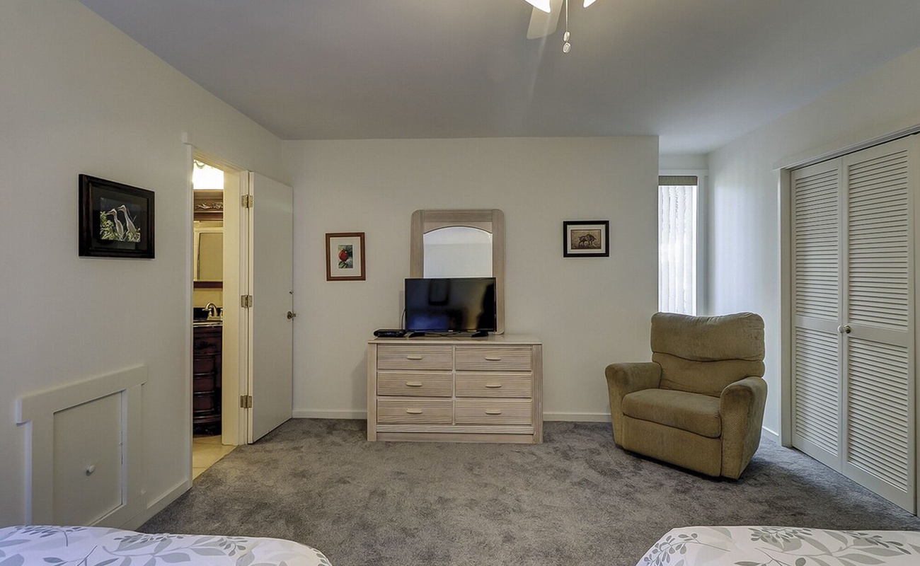 Your spacious bedroom offers comfort with plush carpet, dresser storage, cozy reading chair, and TV for evening relaxation.