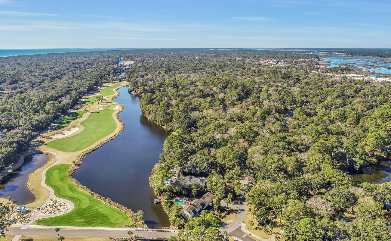 Stunning aerial view showcasing a championship golf course winding along pristine waterways, surrounded by lush coastal forest and nearby ocean views.