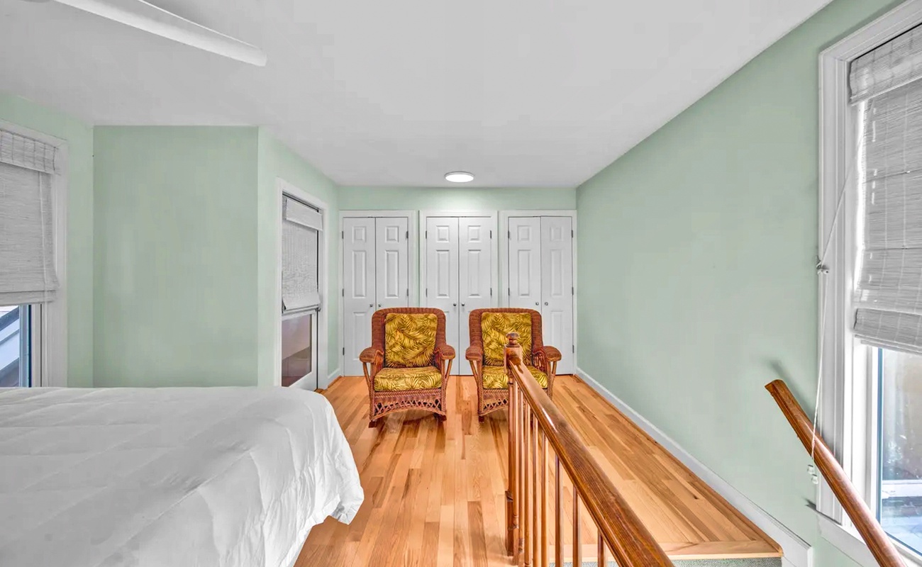 Relax in your serene bedroom with soft mint walls, warm hardwood floors, and charming wicker chairs perfect for morning coffee.