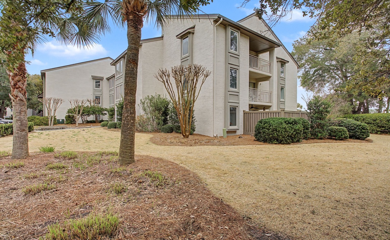 Modern three-story vacation rental building nestled among mature palm trees and lush landscaping in a peaceful residential setting.