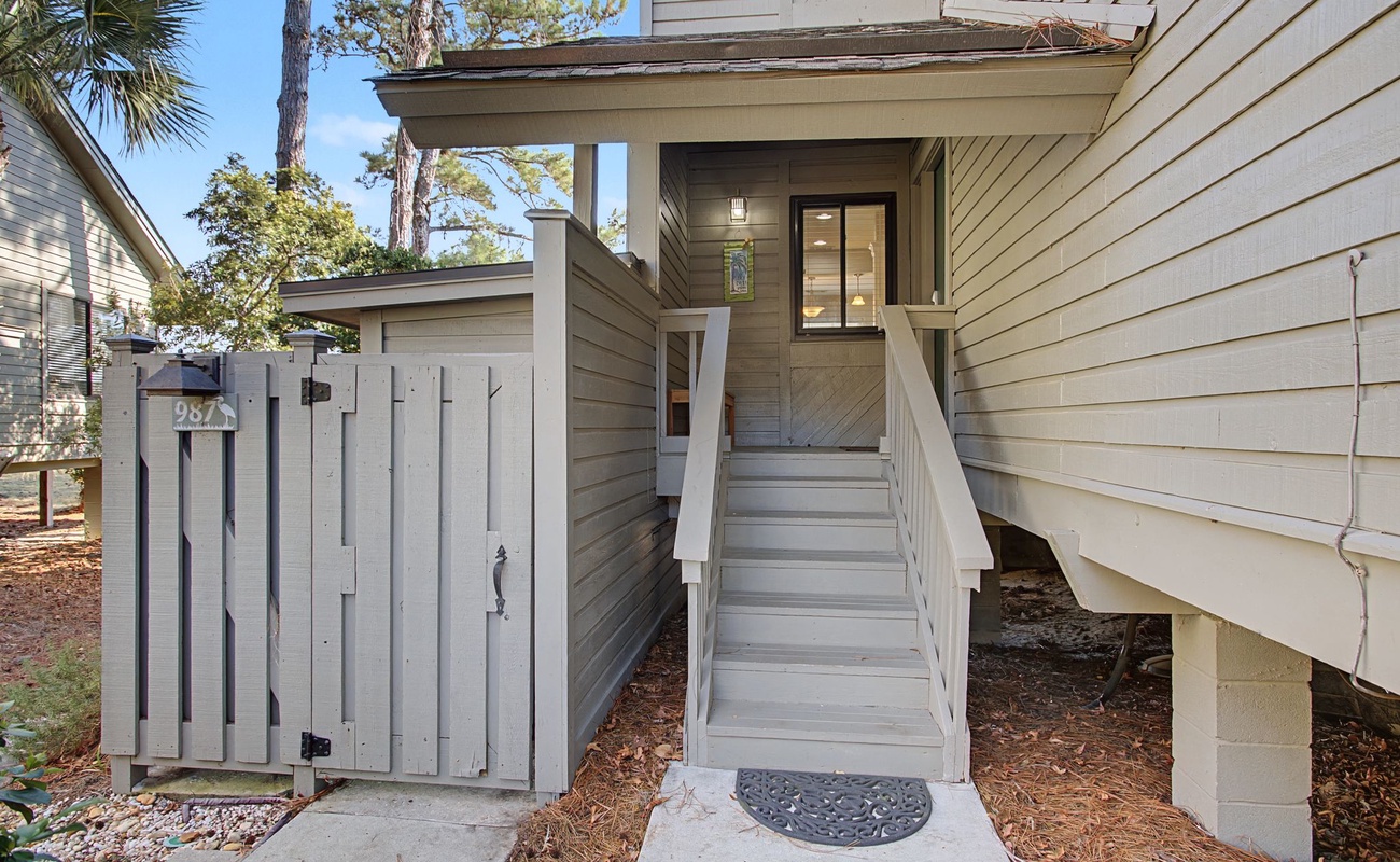 Coastal charm welcomes you at this elevated entrance, where natural wood siding and mature palms create your perfect retreat backdrop.