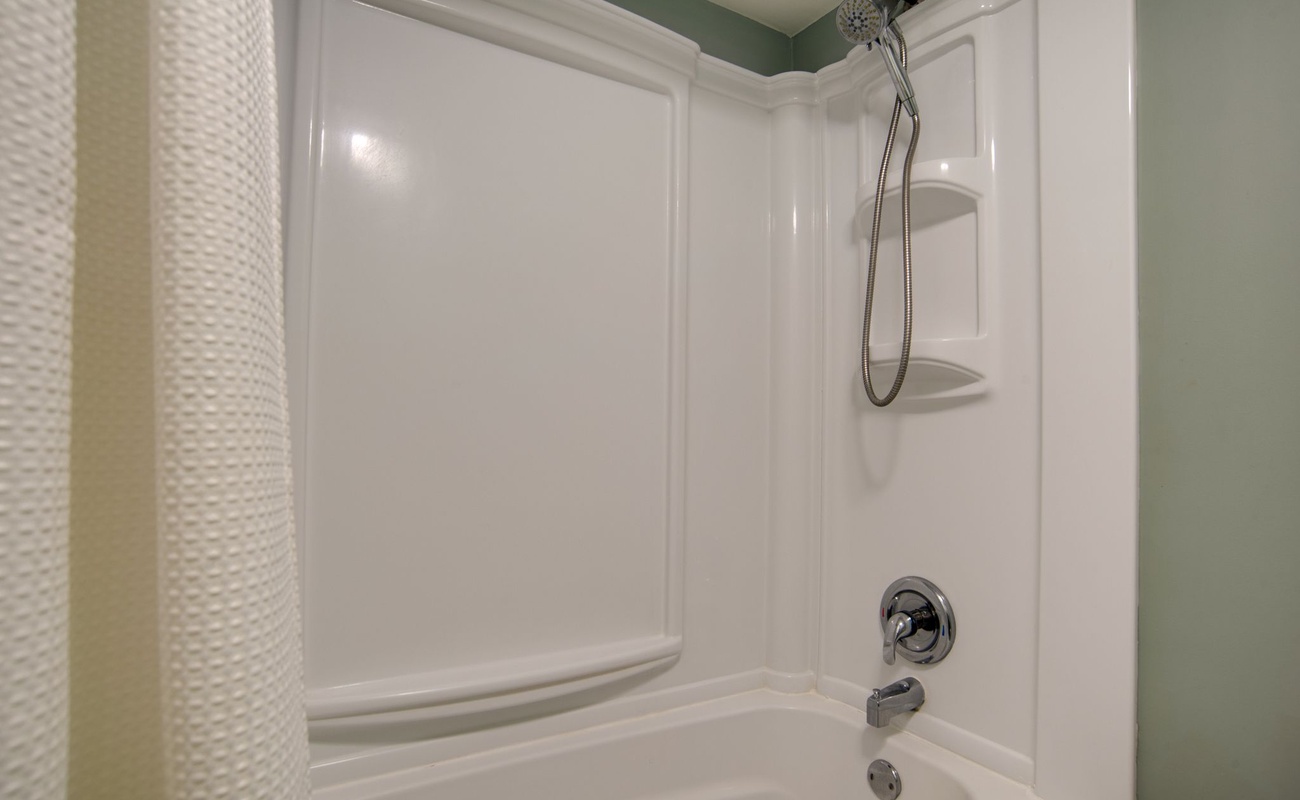 Unwind in your pristine white tub-shower combo with handheld showerhead and convenient corner shelves for toiletries.