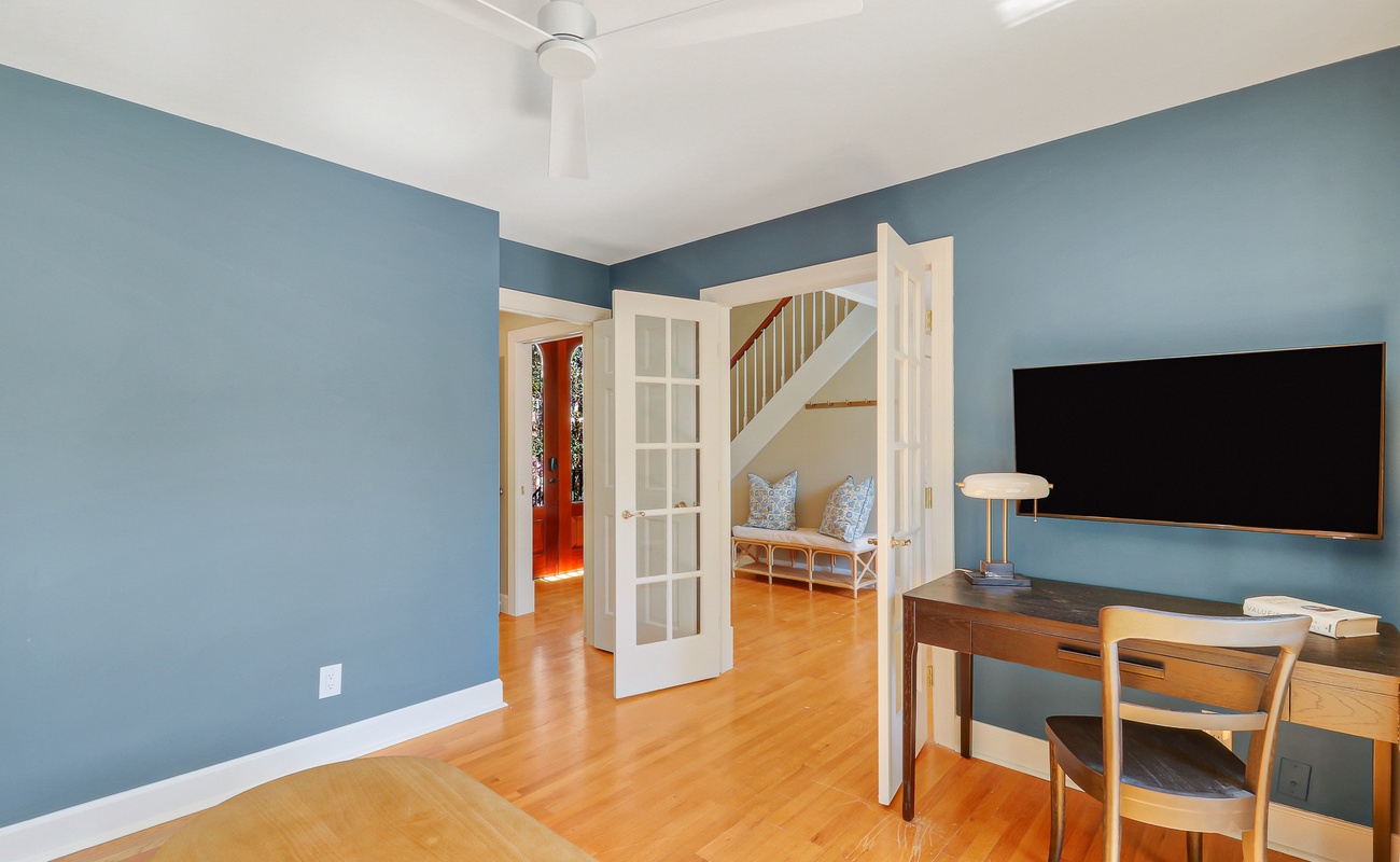 Relax in your stylish living space with calming blue walls, gleaming hardwood floors, and modern amenities including a large TV and workspace.