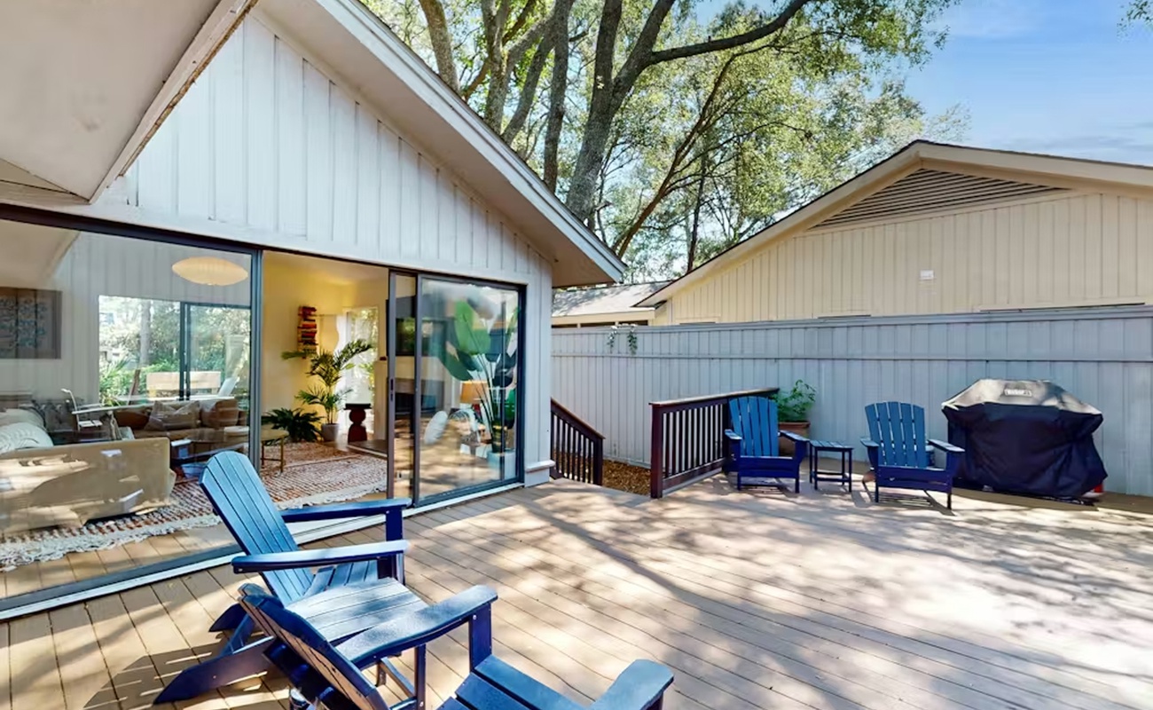 Your private deck offers sun-dappled relaxation with comfy blue chairs and BBQ, seamlessly connecting to bright indoor living spaces.