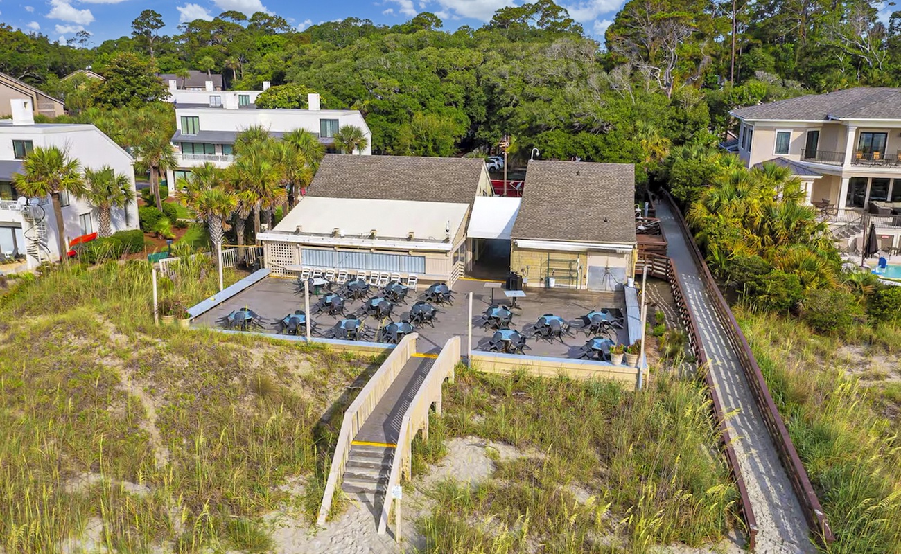 Beachfront property with direct beach access via private boardwalk, surrounded by lush coastal vegetation and nearby residential community.