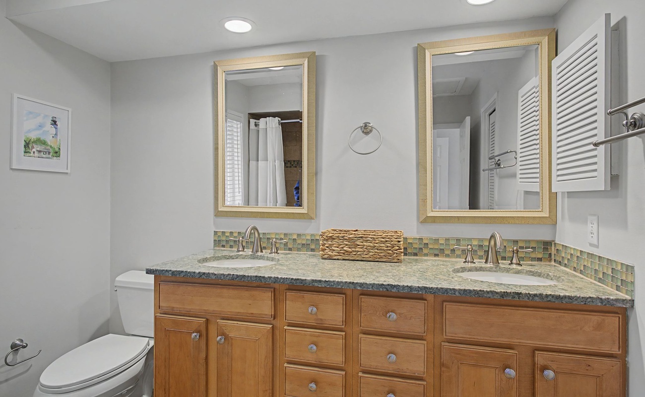 Your spacious dual-sink bathroom features warm wood vanity, granite countertops, and elegant gold-framed mirrors—perfect for your morning routine.