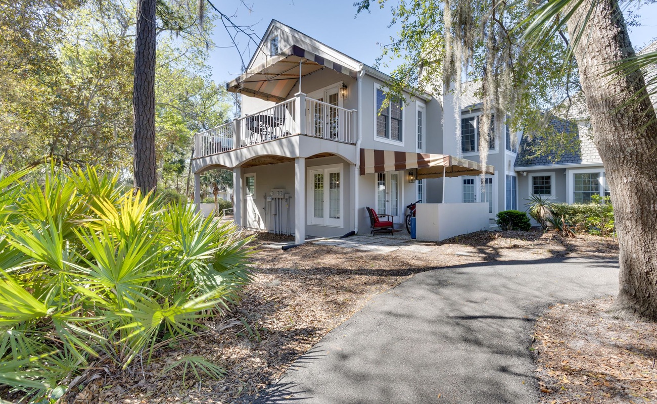 Charming white property nestled among mature trees and tropical landscaping, featuring balconies and welcoming entrance areas.