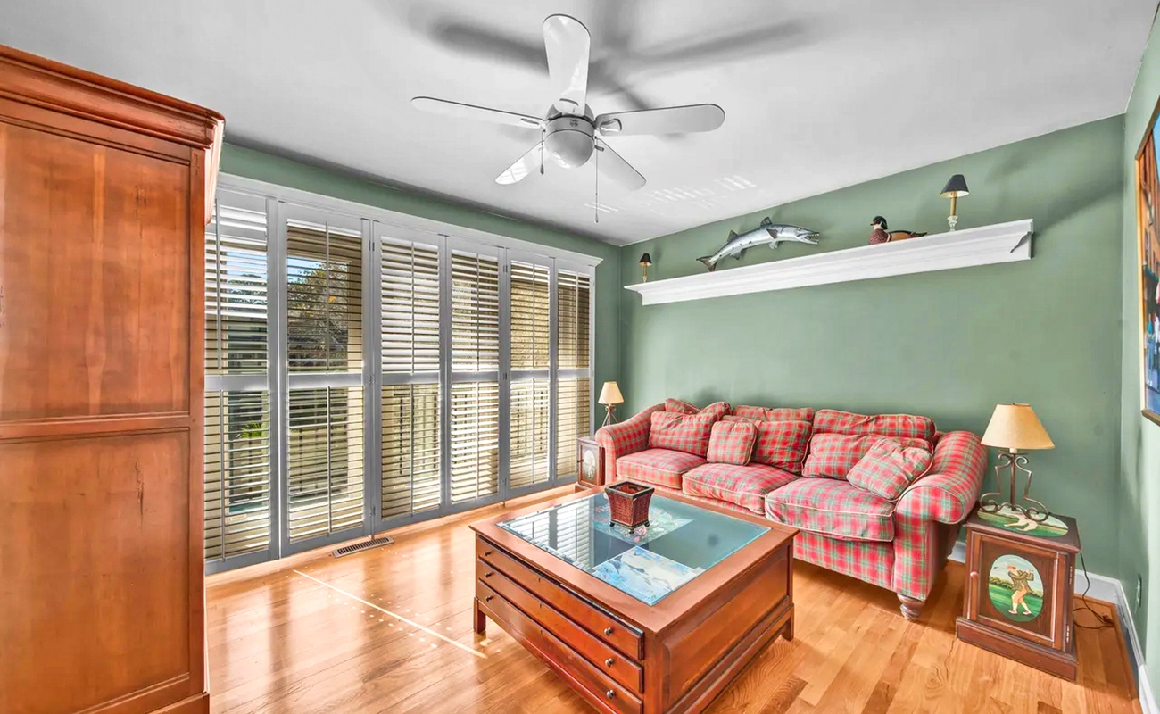 Relax in your cozy living room with warm hardwood floors, plaid sofa, and gentle ceiling fan breeze.