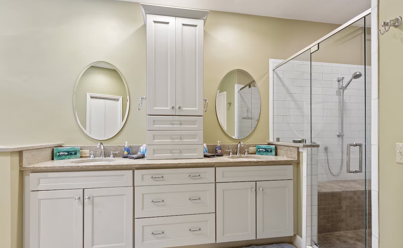 Your spacious bathroom features dual vanities with elegant mirrors and a luxurious glass-enclosed shower with subway tiles.
