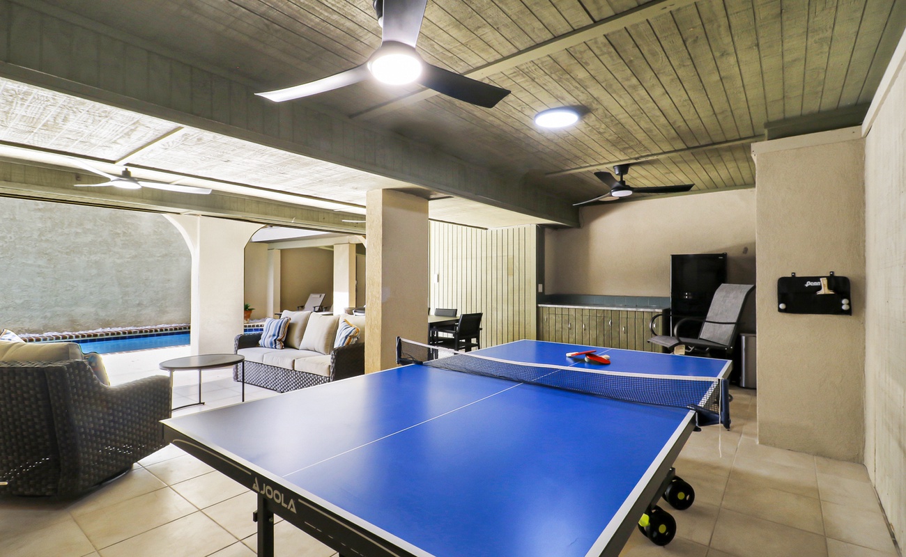 Covered ground-level entertainment space featuring a ping pong table, ample seating, and easy access to the pool - ideal for indoor-outdoor recreation.