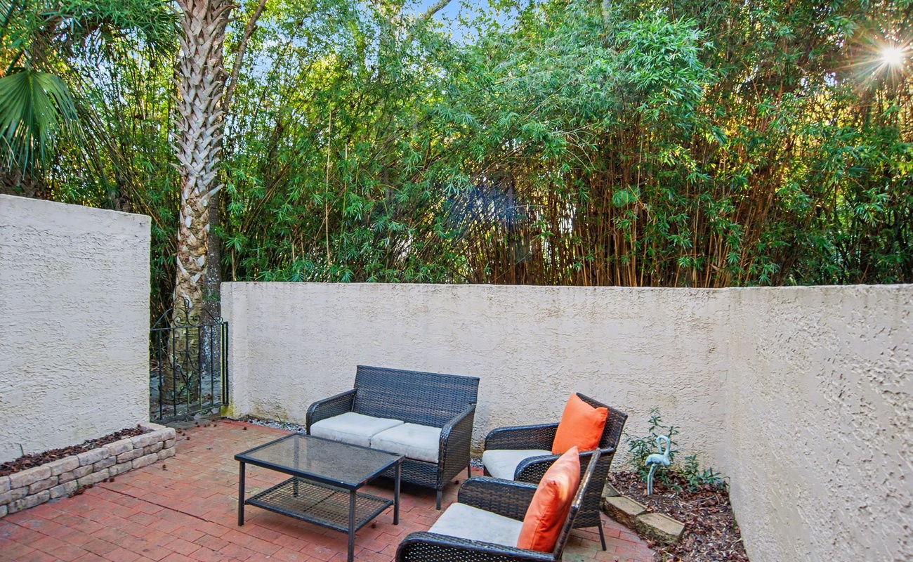 Unwind in your private patio oasis, where wicker furniture and vibrant cushions create the perfect outdoor retreat beneath tropical foliage.