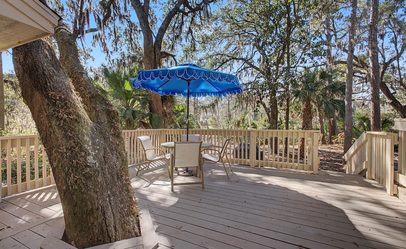 Relax on your private deck surrounded by majestic oaks, where dappled sunlight and a colorful umbrella create the perfect outdoor retreat.