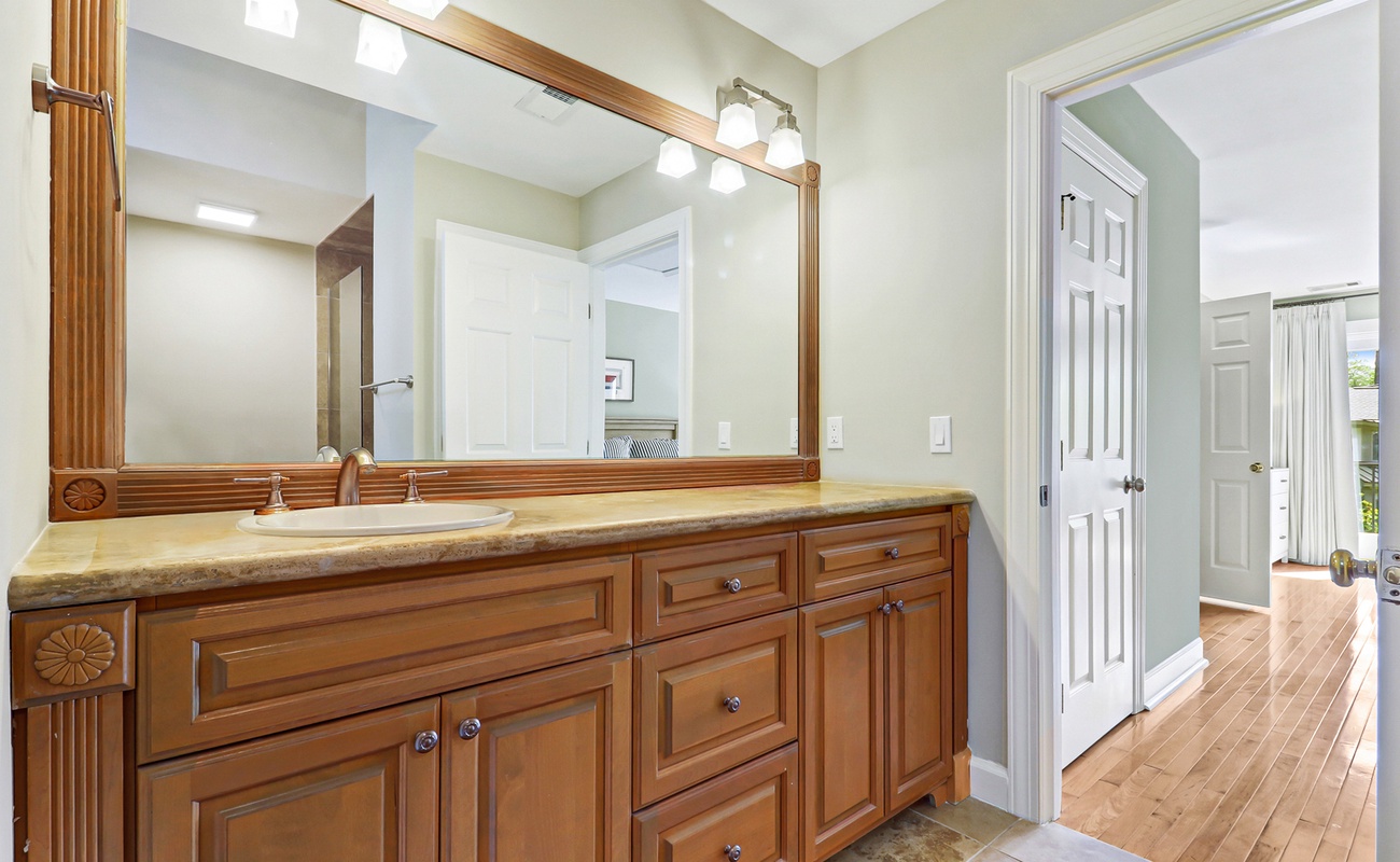Step into your elegant bathroom featuring rich wood cabinetry, granite counters, and bright vanity lighting for your morning routine.