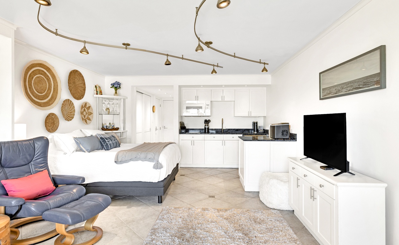 Relax in your bright studio with modern kitchen, cozy seating, and thoughtful touches like woven wall art creating a warm, welcoming atmosphere.