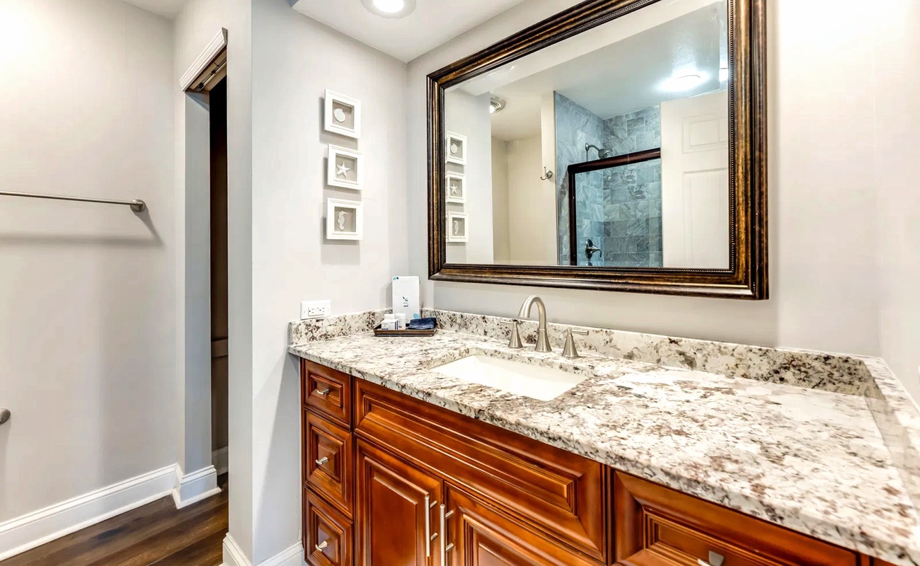 Refresh in your elegant bathroom featuring granite countertops, rich wood cabinetry, and a pristine marble-tiled shower behind you.