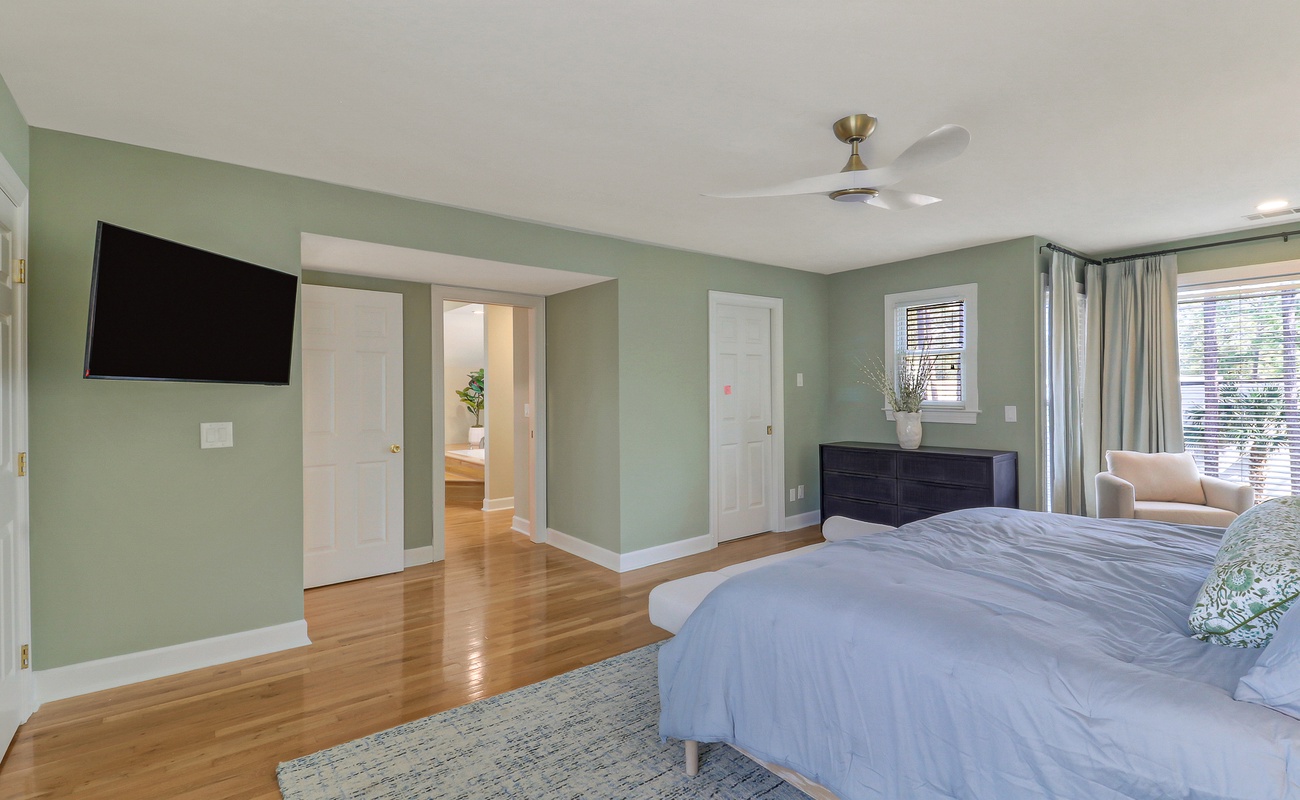 Unwind in your spacious master suite with soothing sage walls, gleaming hardwood floors, and modern amenities including ceiling fan and wall-mounted TV for ultimate relaxation.