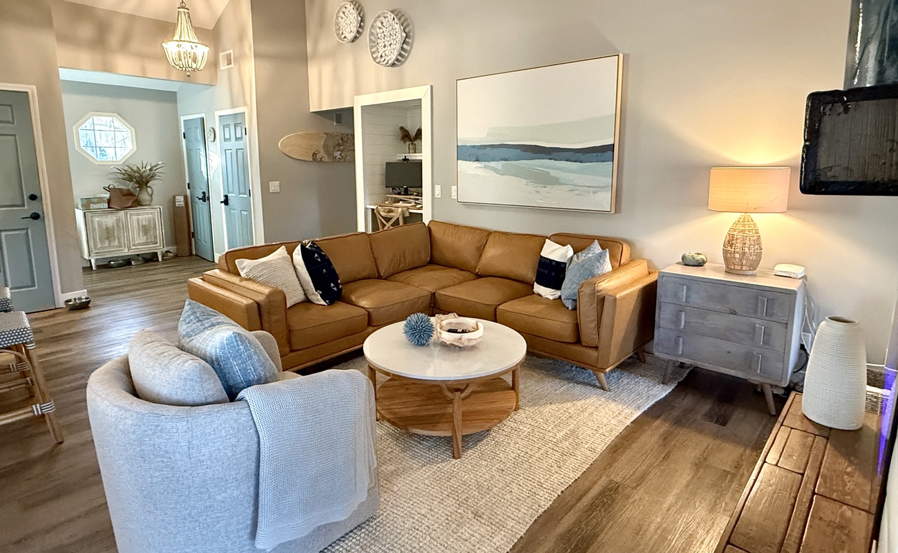 Sink into plush leather seating in your coastal-inspired living room, where warm wood floors and ocean artwork create the perfect retreat.