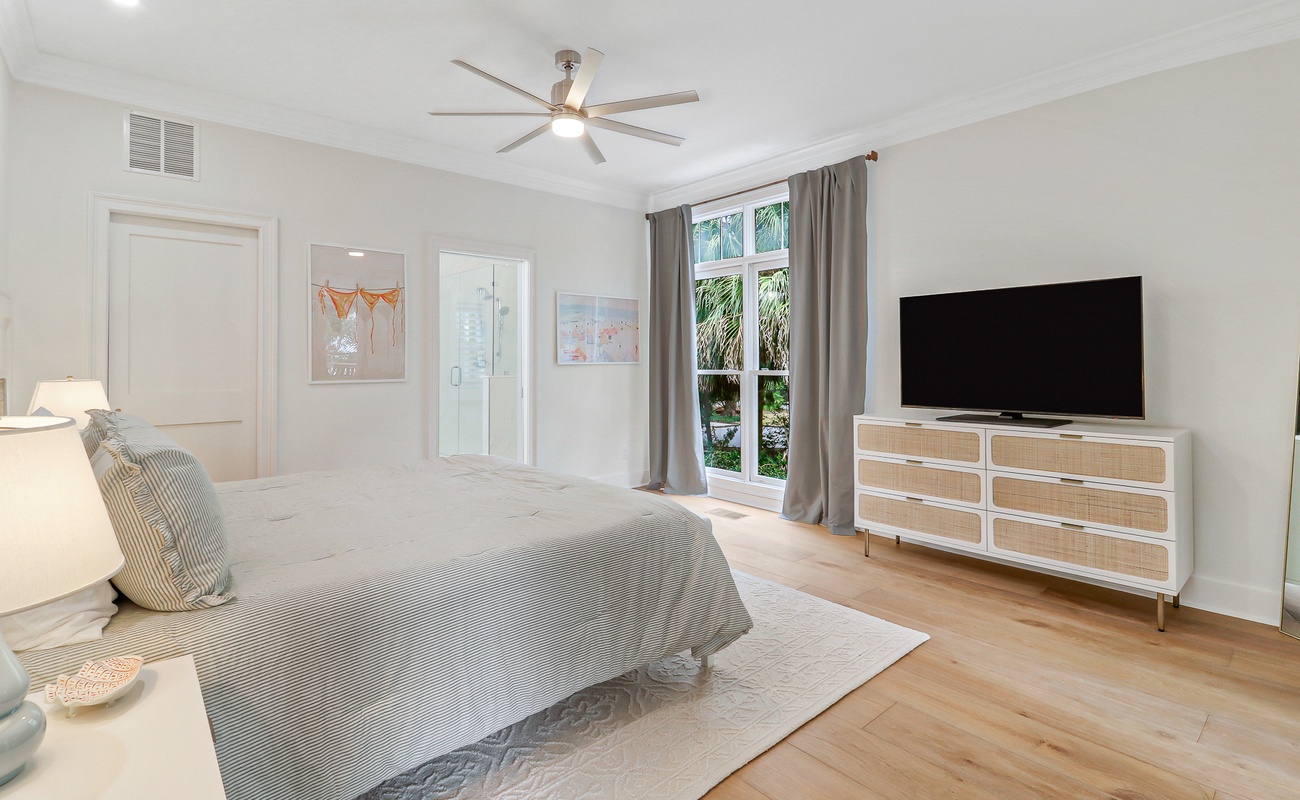 Unwind in your serene master bedroom with ceiling fan comfort, garden views through French doors, and modern entertainment center for perfect relaxation.