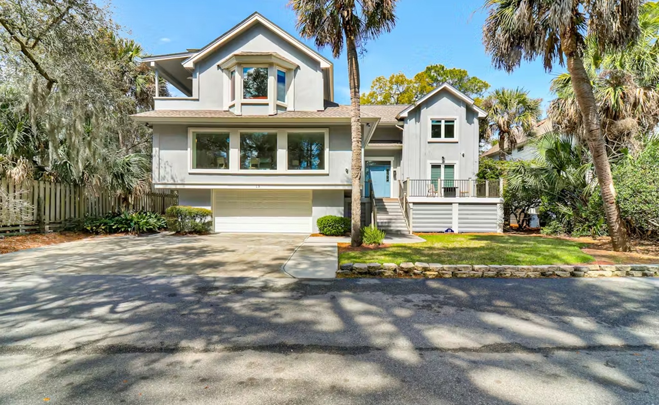 Modern coastal home nestled among towering palms and lush landscaping on a quiet residential street.