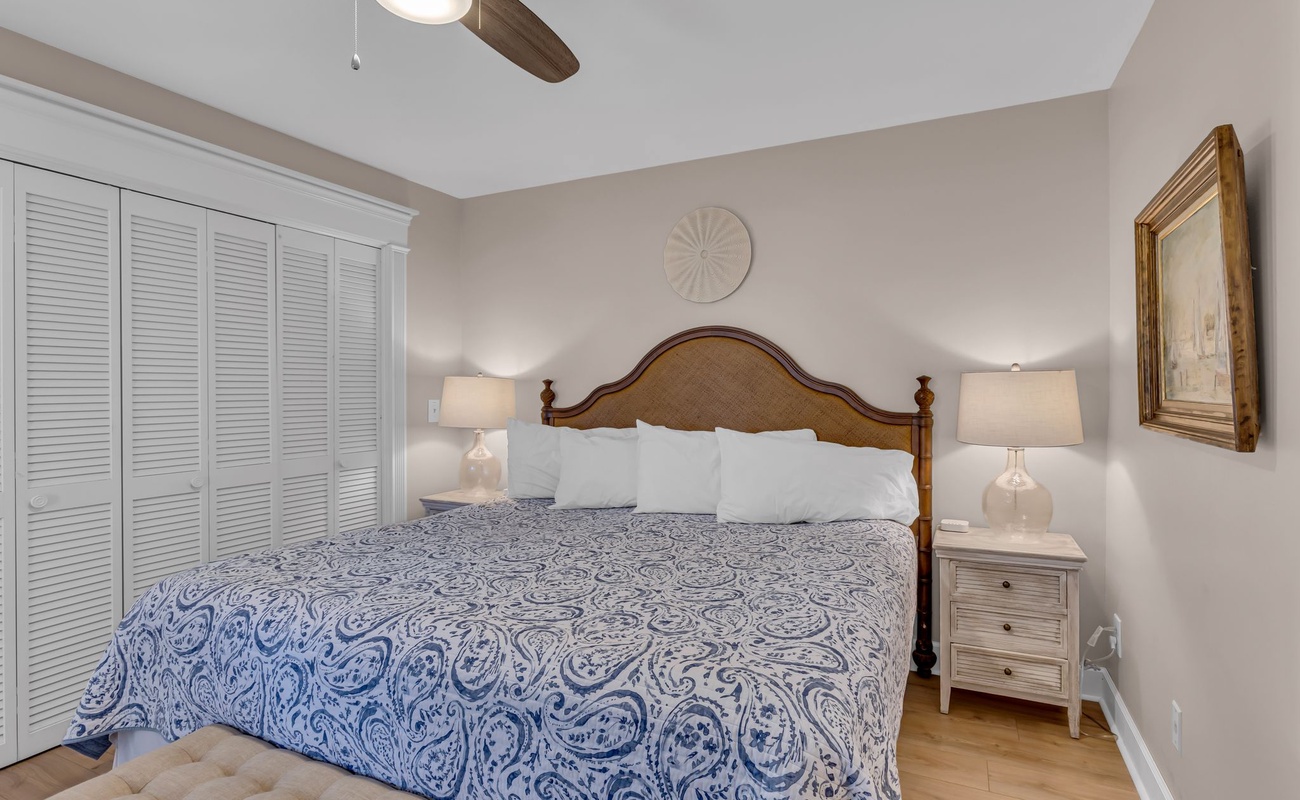 Drift off to peaceful sleep in your elegant bedroom, featuring a plush king bed with coastal-inspired linens and gentle ceiling fan.